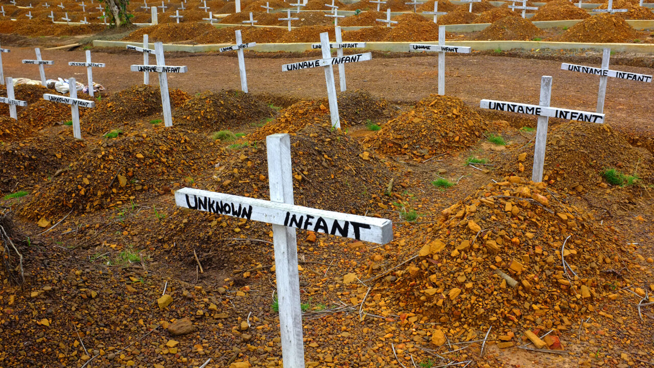 A photo of a graveyard marked by white crosses reading "unknown infant"