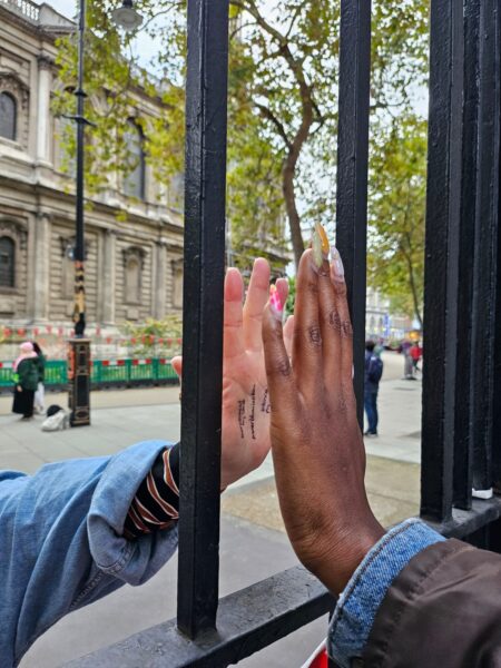 A Black person and a white person touching their hands to either side of a glass window