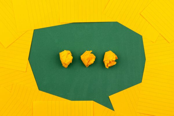 Yellow paper arranged to shape a speech bubble on a green background, with three dots in the speech bubble