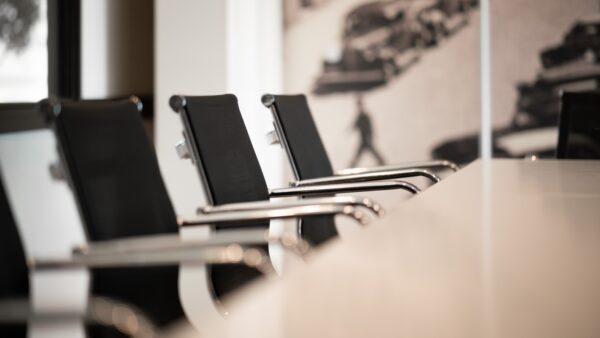Close up shot of a row of black, smart chairs lined up along a table, evocative of a committee meeting