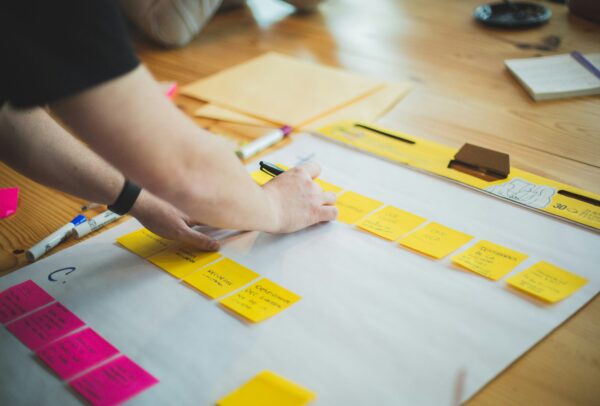 hands of a person writing on on post-it notes stuck to a big piece of paper on a table